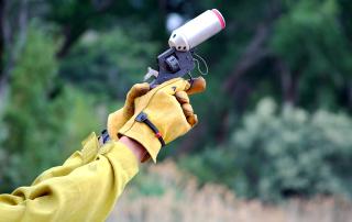 A firefighter trainee grips a pistol-style flare launcher with a gloved-hand as she takes aim over an unseen firing range.