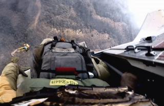 Skydiver at edge of open door, ready to exit the plane with smoke in the hills below.