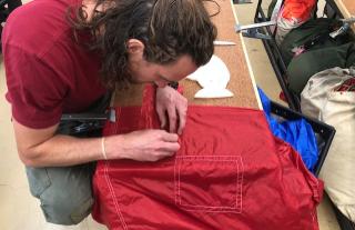 Smokejumper Cole Skinner patches a ripped parachute.