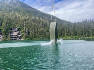 A helicopter lowers one end of a boat into the lake.