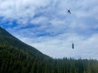 A helicopter transports a boat, which dangles below on wires.