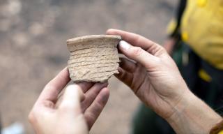 An ancient corrugated pottery sherd held by two hands.