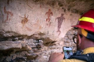 A wildland firefighter using a smartphone to take a picture of an ancient petroglyph panel in front of him.