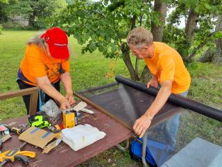 Volunteers building custom window screens at an outdoor workspace.