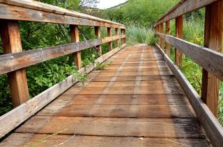 A wooden bridge with alternating dark and sun faded lines on the planks showing where large wear boards used to run the length of the bridge.