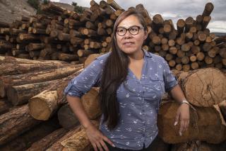 Hispanic woman stands in front to stacked logs