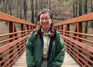 young woman wearing forest service uniform stands on bridge