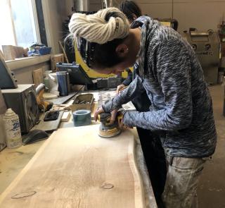 Young woman using circular sander to sand a large piece of wood