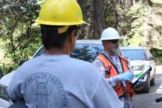 Two employees with hardhats discuss pheromone technology on site in the Tahoe National Forest.