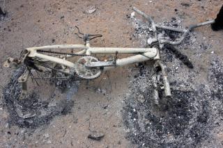 Image of charred bicycle with burned wheels on the ground blackened by fire