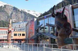 In foreground, is mask representing Tlingit, Haida and Tsimshian peoples of Southeast Alaska. Behind it is the Sealaska Heritage Foundation and other buildings of downtown Juneau.