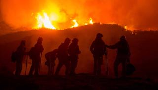 A group of firefighters silhouetted against a fire on the horizon.