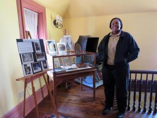 A'Precious Norfleet, in Forest Service uniform, stands next to a glass display case and easel with historical photos in a room at Grey Towers.