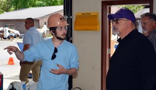 A young man in a hard had talking with an older man in a ballcap