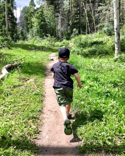 A child running away from the camera, down a dirt path in a forest.