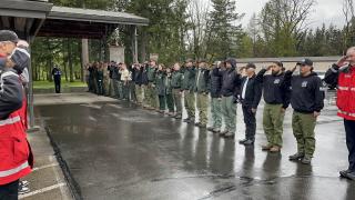 Employees, some in uniform, line both sides of a walkway and salute. A Forest Service honor guard member holds the folded American flag and appears ready to walk through the line.