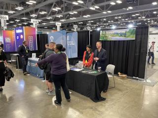 Employees stand behind a table in a cavernous room. Behind them hangs a Forest Service National Partnership Office banner.
