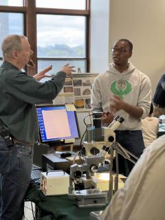 Earth Day event attendee listens to a Forest Products Lab employee in area with microscope and computers.