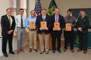 Group photo: engineering of year award recipients holding their plaques. They are in a conference room in front of American and Forest Service flags.