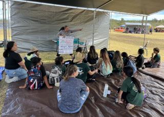 A group of children sitting on the ground under a tent