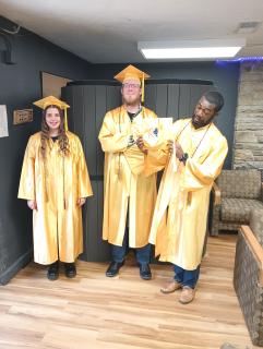 A young woman and two young men, wearing gold-colored graduation caps and gowns pose for a photo.