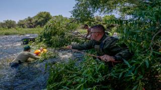 A law enforcement officer in the river helps the law enforcement officer in tree branches use a rope to rescue a stranded tuber.