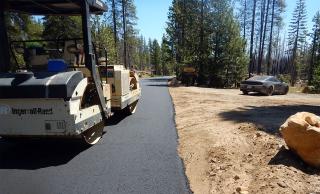 Large drum roller sits on a freshly paved asphalt with dirt cut-out to the right.