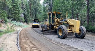 road construction equipment laying pavement along a forest road path.
