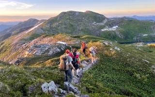 A group of people hiking a trail that runs along a mountain ridgeline.