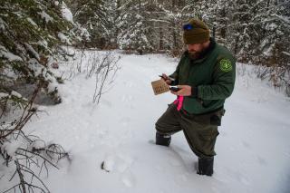 A man standing in the snow, collecting samples.