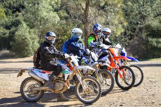 Image shows four dirtbikers in their gear and sitting on their bikes, looking at the camera.