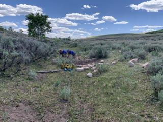 Image shows two people working on a stone structure surrounded by prairie.
