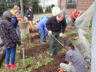 Image shows a group of people doing gardening work outside a log cabin.