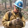 Wildland firefighter Nickolas Brasher in the forest holding a small animal.