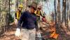 Woman holding a drip torch, ignites ground vegetation during a prescribed fire event.