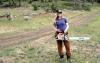 A pregnant woman wearing baseball cap holding chainsaw in the woods.