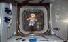 Image shows a doll of Smokey Bear floating in front of an open hatch inside the International Space Station.