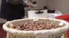 Brown Emory oak acorns gathered in a bowl are in the foreground, while someone ladles a bowl of soup in the background.