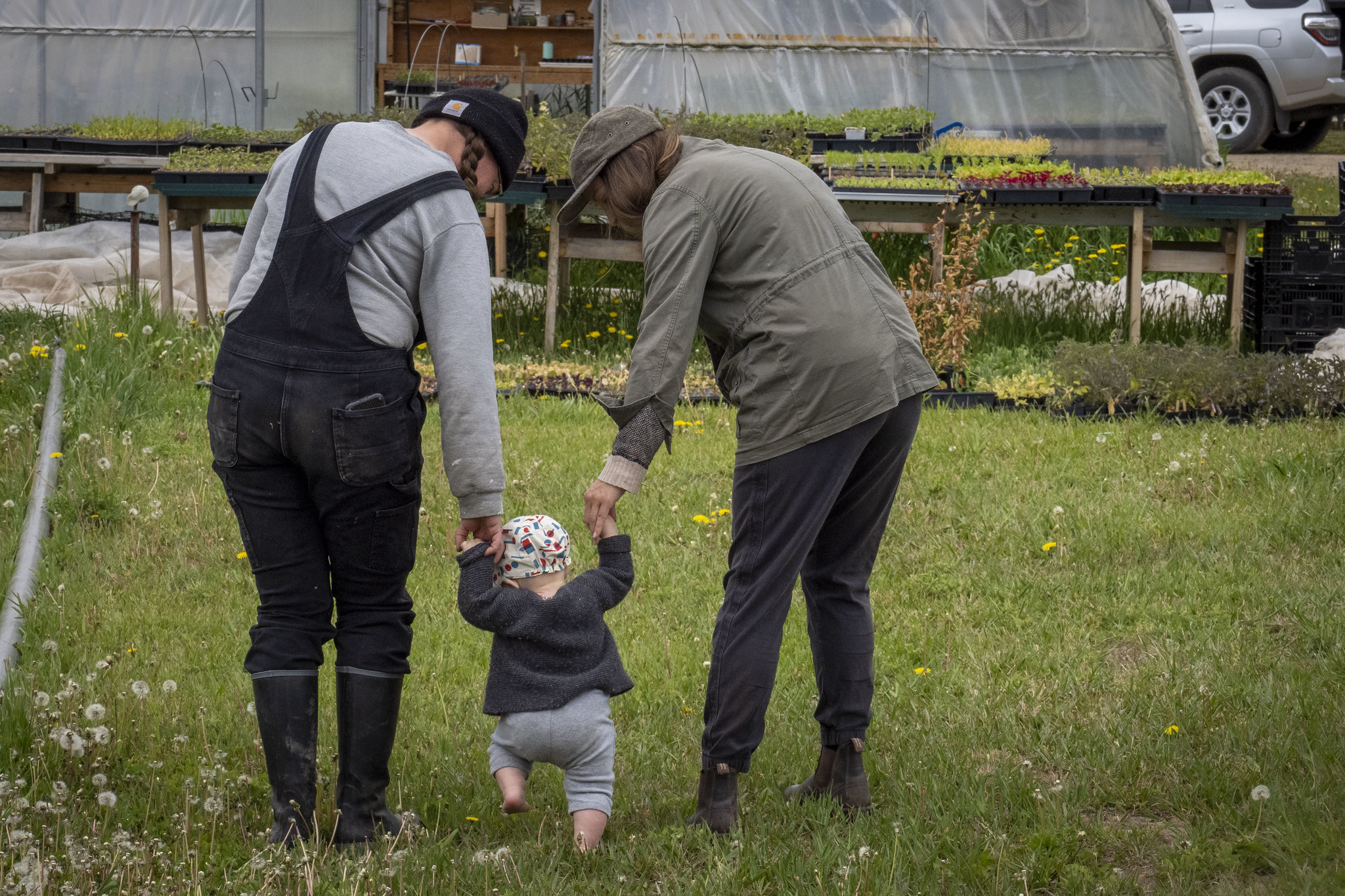 Two people hold hands with a child walking toward a greenhouse.