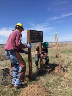 Two people repair or install a trail sign in the grasslands.