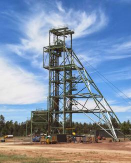 A metal mining structure rises above bare ground with trees in the background.