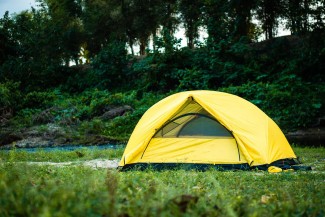 Yellow Tent in a green field with trees in the background.