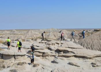 A group of people are walking along a trail through unique formations in Toadstool Geological Park.