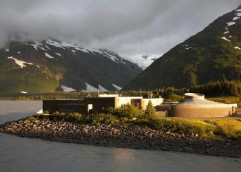 The Begich, Boggs Visitor Center, sitting on a glacial lake with snow-capped mountains in the background.