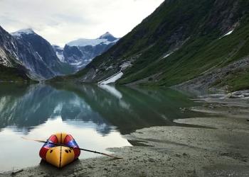 A pack raft at the edge of the water in a steep glacial valley.