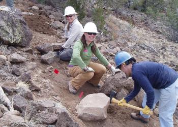 A group of archaeology volunteers dig around boulders on a hillside