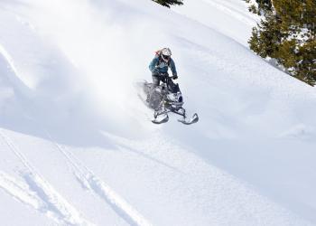 A snowmobile jumps in the air over a pristine field of snow.