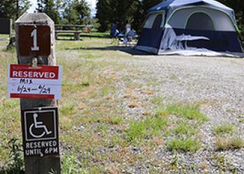 A photo of a campsite, reservation post states, 1, reserved. A tent and picnic table in the background.