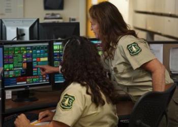 A photo of two women at a computer workspace looking at a computer. One woman is pointing at the screen.