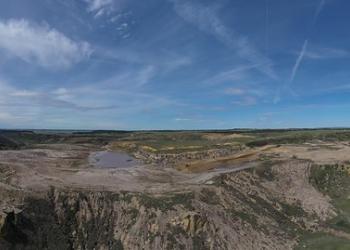 A photo of a view of a land area that has a mine in the center and a small body of water near the middle of the photo.